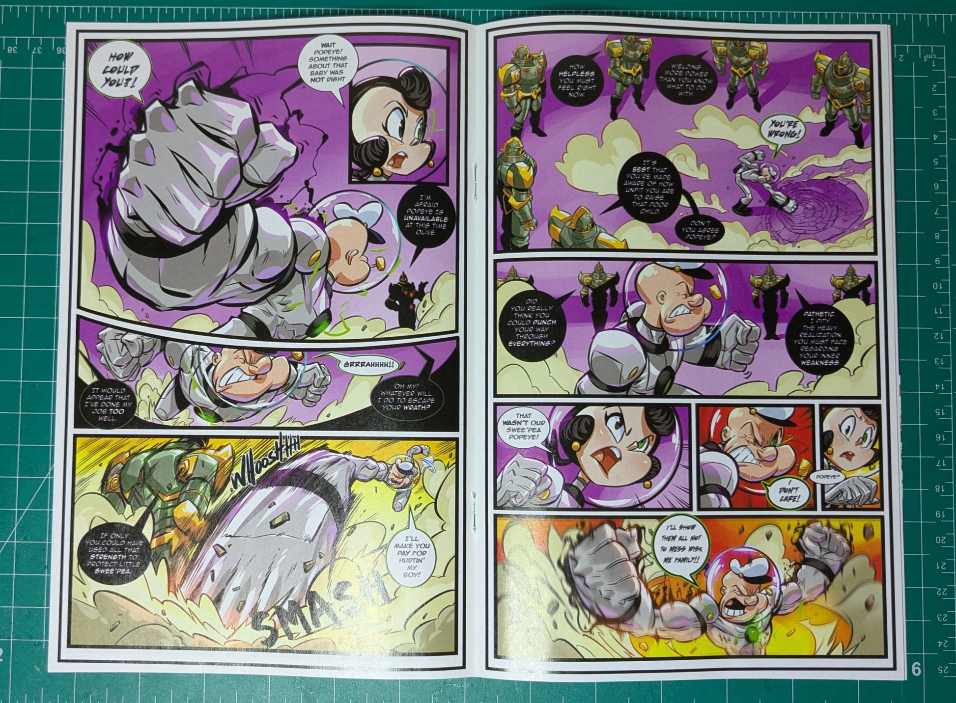An open printed comic book or manga page laid flat on a green cutting mat. The page contains multiple illustrated panels with a purple, yellow, gray, and black action scene, speech bubbles, and character faces.
